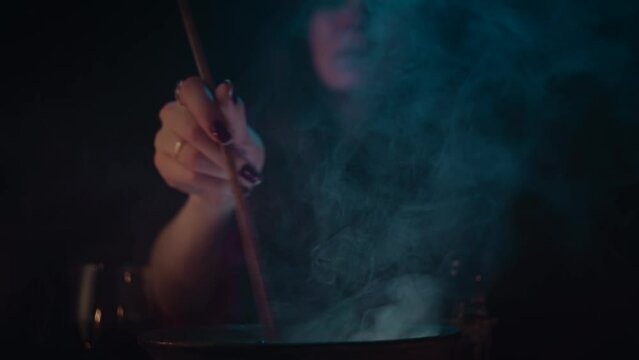 Halloween theme: Young witch cooking in cauldron, slow motion. Close up to cauldron 