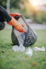 Male hand picking up plastic waste to clean up at the park.