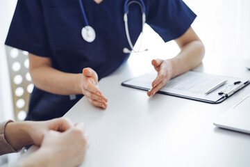 Doctor and patient sitting at the table in clinic while discussing something. The focus is on female physician's hands, close up. Medicine concept