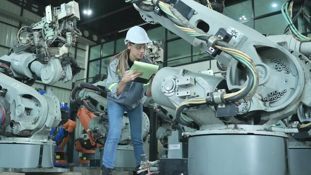 A female engineer checking documented items after installing a program on a robotic arm in a robotic warehouse and test the operation