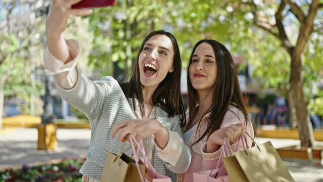 Two women going shopping holding bags make selfie by smartphone at park