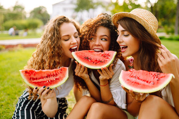 Three beautiful young girls have fun together and eating watermelon in hot day. Summer, lifestyle, travel, nature and vacations concept.