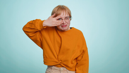 Nosy curious young woman in glasses closing eyes with hand and spying through fingers, hiding and...