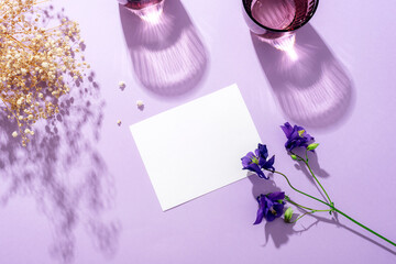 Modern summer stationery still life. Two glasses of water with long shadows and blue flowers on purple background. Blank business card mockup. Top view, flat lay