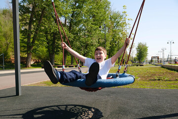 Cute boy is riding on a swing on the embankment.