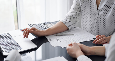 Woman accountant using a calculator and laptop computer while counting taxes for a client. Business...
