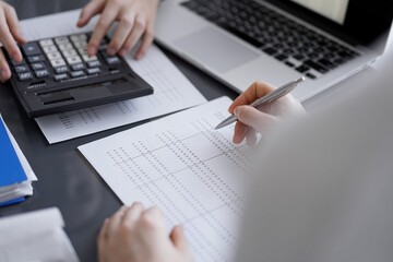 Woman accountant using a calculator and laptop computer while counting taxes for a client. Business audit concepts