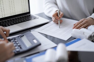 Woman accountant using a calculator and laptop computer while counting taxes for a client. Business...