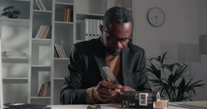 Portrait of a watchful afro-american male architect measuring a tiny house model