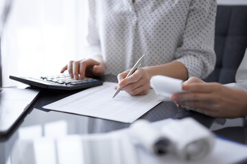 Woman accountant using a calculator and laptop computer while counting taxes for a client. Business...