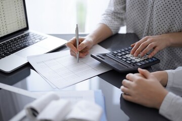 Woman accountant using a calculator and laptop computer while counting taxes with a client or...