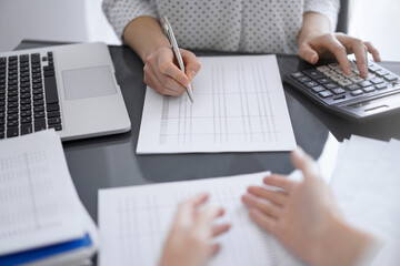 Woman accountant using a calculator and laptop computer while counting taxes with a client or...