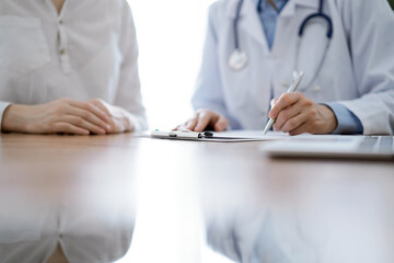 Doctor and patient discussing something while sitting near each other at the wooden desk in clinic, view from above. Medicine concept