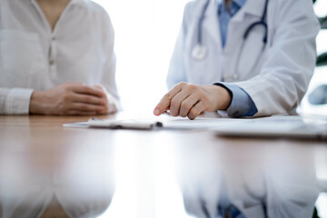 Doctor and patient discussing something while sitting near each other at the wooden desk in clinic, view from above. Medicine concept