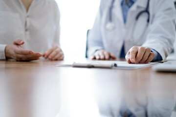 Doctor and patient discussing something while sitting near each other at the wooden desk in clinic, view from above. Medicine concept