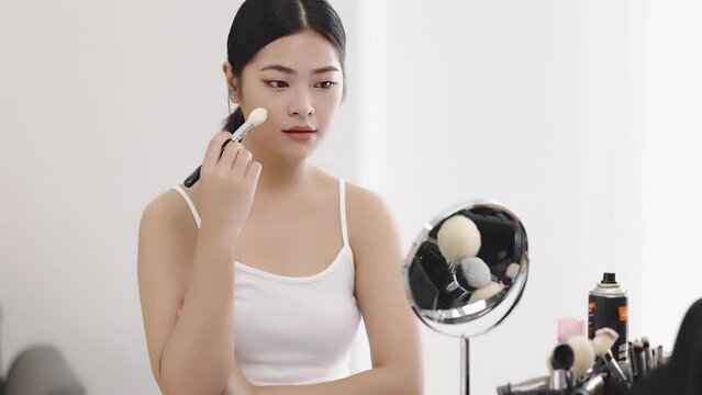 Slow motion shot Close up beauty young pan Asian woman looking at a mirror and applying cosmetics on healthy skin face.