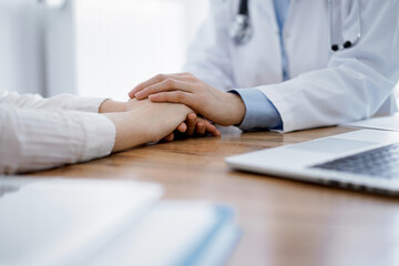 Stethoscope and tablet computer are lying on the wooden table while doctor's hands reassuring a patient at the background. Medicine concept