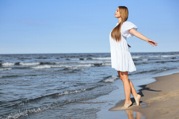 Happy smiling beautiful woman is on the ocean beach in a white summer dress, open arms