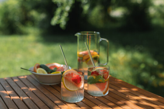 Still life of two summer drinks with fresh fruit on a table in dappled light in the garden