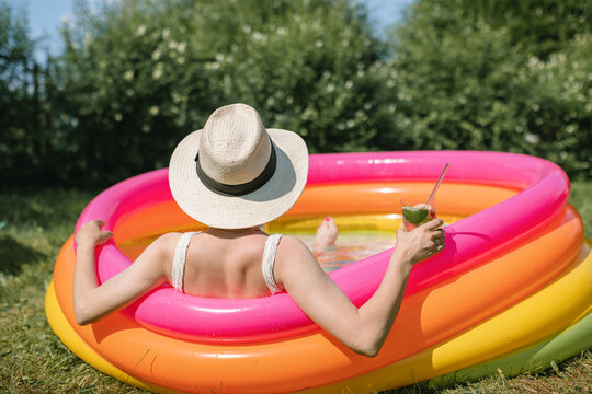 Rear view of a woman sitting in a paddling pool in summer with a refreshing fruit drink