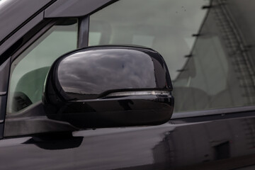 Close-up of the side left mirror with led turn signal and window of the car body black SUV on the street parking after washing and detailing in auto service industry. Road safety while driving
