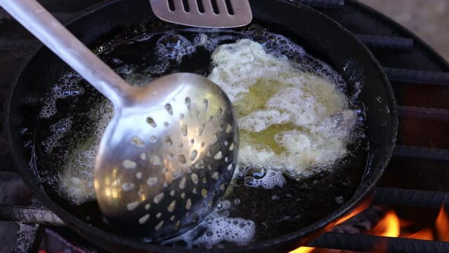 Unrecognizable latin farmer person cooking fried hake fish in a frying pan, on a metal grill with red hot firewood