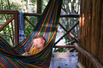 Boy lost in his thoughts in a hammock in a tropical setting