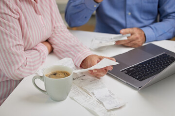 Close up of couple hands checking their bills and receipts sitting at home with laptop. Husband and wife having problems with finances or struggling with paying the bills online