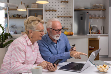 Excited and happy elderly couple shopping online from home using computer, smartphone and credit card. Modern technologies and retirement concept.