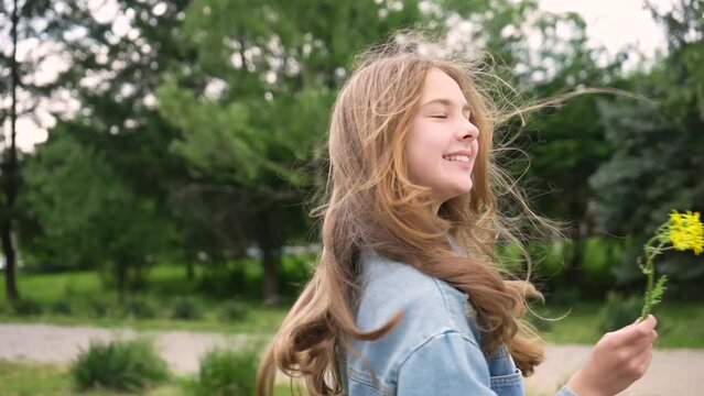 Smiling teenage girl with yellow flower in hand turns to camera walking in park