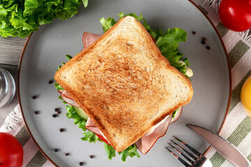 Delicious ham sandwich with fresh salad and tomatoes served on plate. Top view.