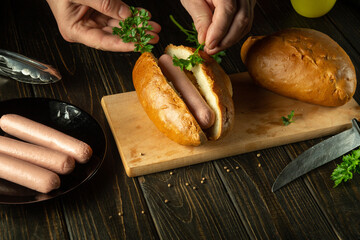 Cooking hot dogs by the hands of a chef on the kitchen table. The concept of cooking fast food or street food