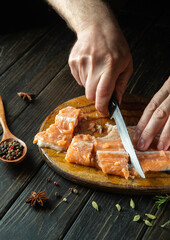 The chef cleans red fresh fish on a wooden cutting board with a knife. Home cooking of a delicious fish dish according to an old recipe.