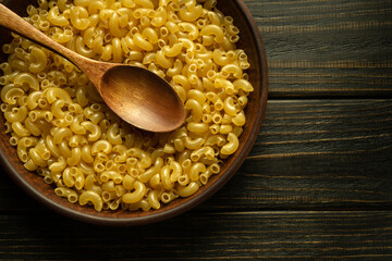 Vintage plate and spoon with raw pasta before cooking national dish on a dark kitchen table. Diet and healthy food