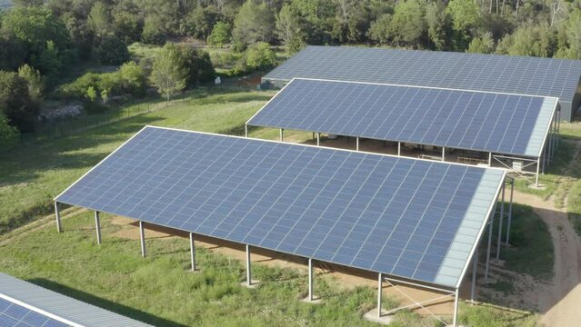 Aerial shot that reveals a small solar panel farm in the forest with barns and a shed
