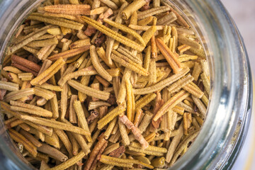 Dry rosemary leaves inside glass jar closeup