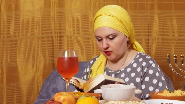 A Jewish woman at a covered Shabbat table reads a siddur prayer.