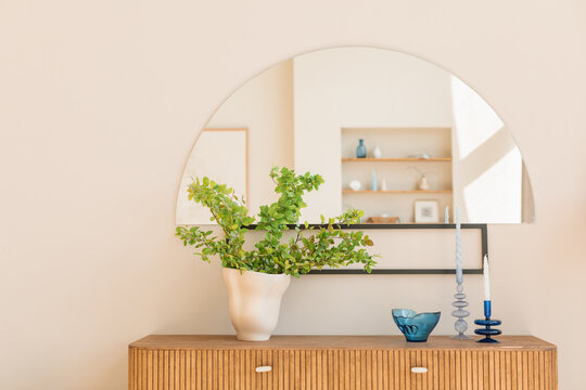 Candlesticks, glass bowl and green branches in trendy vase on a modern sideboard in a living room