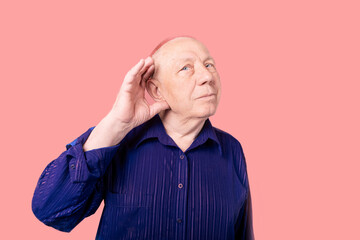 an elderly man in a blue shirt put his hand to his ear. he listens badly. eavesdropping. white...