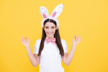 Obraz na płótnie Canvas Happy Easter. Portrait of young smiling woman with bunny ears isolated on yellow studio background. Easter bunny woman looks fun. Rabbit girl pointing on copy space.
