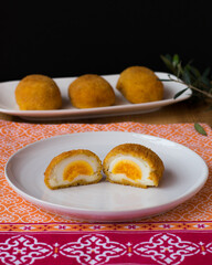 Huevos cocidos fritos servidos en plato blanco sobre mantel colorido y fondo negro. Fotografía vertical.