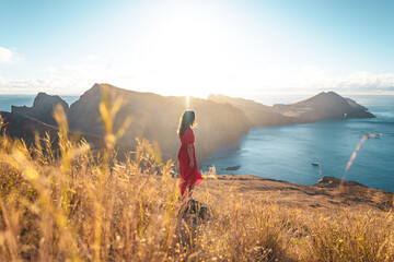 Woman in red dress sunbathing with scenic view on the foothills of a volcanic island in the...