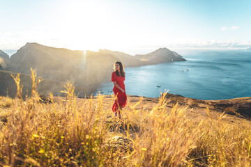 Fototapeta premium Elegant woman in red dress enjoys the morning atmosphere from the foothills of a volcanic island in the Atlantic Ocean. São Lourenço, Madeira Island, Portugal, Europe.