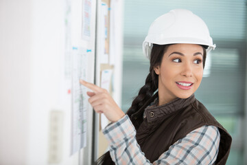woman wearing a safety helmet pointing to notice board