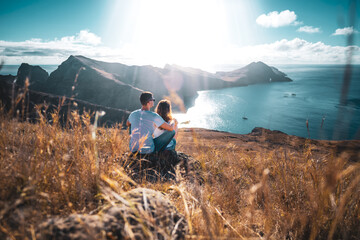 Back view of a tourist couple sitting on a hill, overlooking the coastal landscape of Madeira...