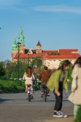 Obraz premium A couple, a man and a woman, ride bicycles on a bike path on a sunny spring evening in Krakow against the backdrop of the Wawel Royal Castle, bike date, eco-friendly transportation, genuine stability
