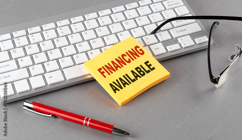 Poster financing available text on a sticky with keyboard, pen glasses on grey background