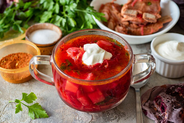 Family lunch. A dish for the whole family for dinner: borscht with pork, vegetables and sour cream in a beautiful plate on a gray background. Beetroot soup. Russian cuisine. Close-up.