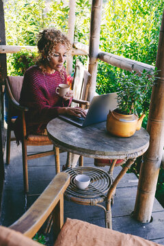 Healthy serene woman sitting outdoor at home in patio with green nature background and using laptop with wireless connection. Concept of alternative office and job. Surfing the net leisure person