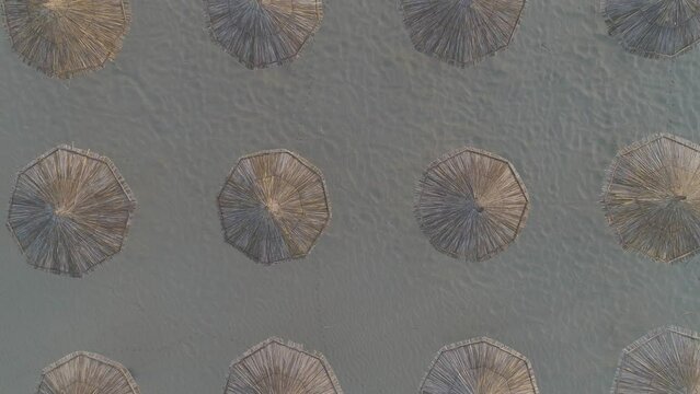 Aerial footage of wicker parasols lined at a beach, the shot is moving up